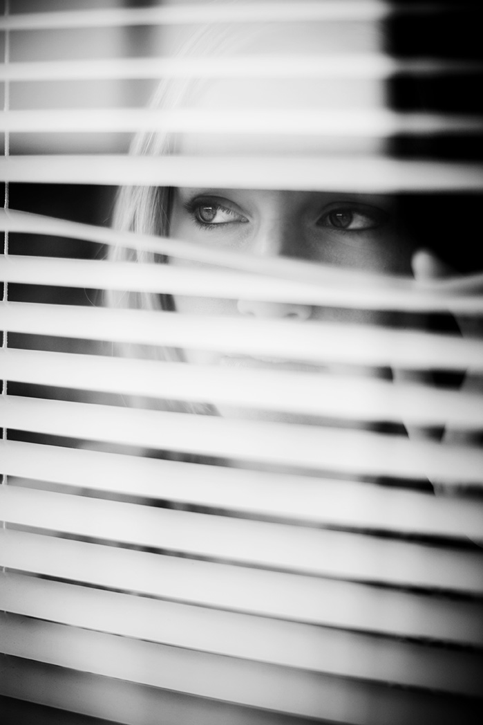 Young Woman Looking Through Window Blinds